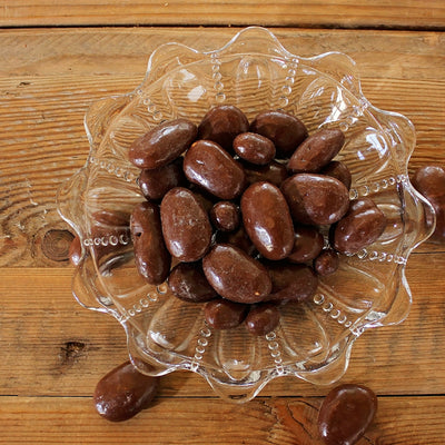 Dark chocolate covered pecans in bowl on wooden table